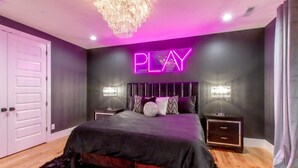 A bedroom with a bed, nightstands, a chandelier, and a neon 'PLAY' sign on the wall. - Playmate Lounge - Glam Rooftop Retreat | Hot Tub, Putting Green & Skyline Views (Nashville)