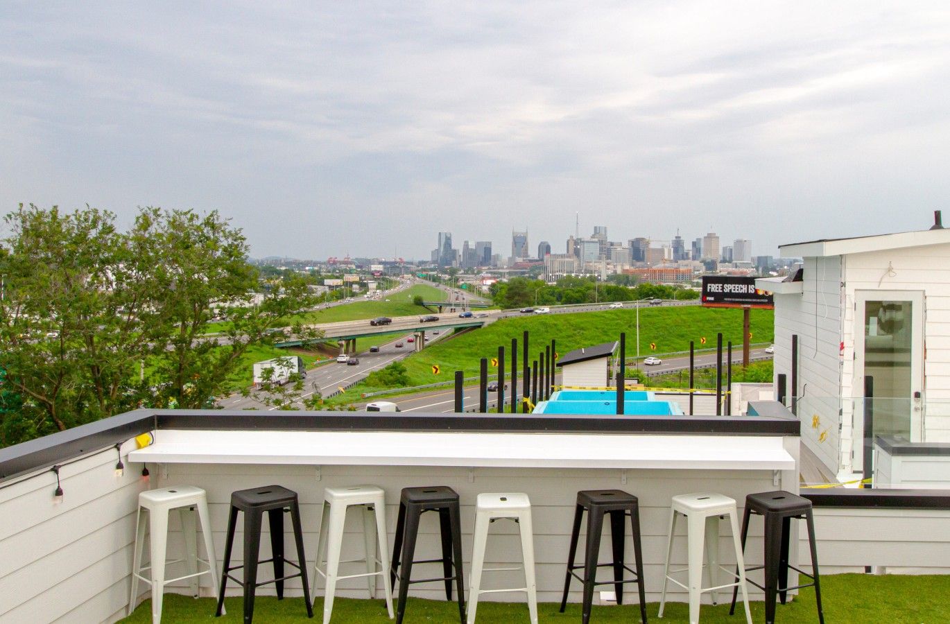 A rooftop bar with a city skyline view, multiple bar stools, and a sign indicating free speech.