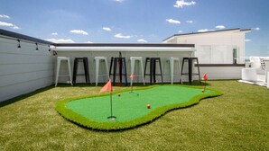 A miniature golf course with artificial turf, flags, and stools arranged around it. - Playmate Lounge - Glam Rooftop Retreat | Hot Tub, Putting Green & Skyline Views (Nashville)