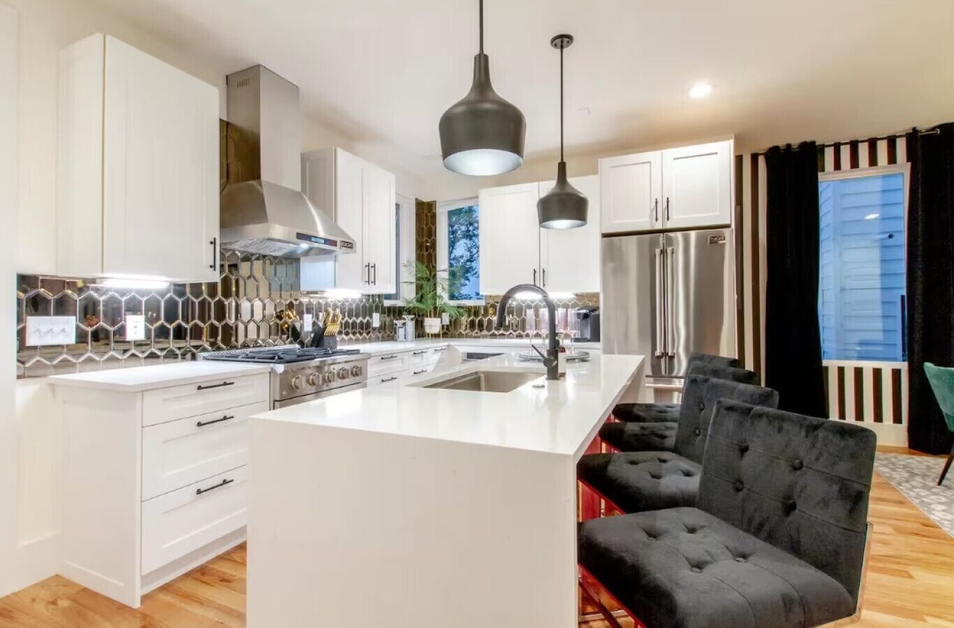 A modern kitchen with white cabinetry, a central island, pendant lighting, and a dining area with black upholstered chairs.