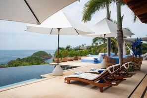 A poolside area with lounge chairs and umbrellas, overlooking a body of water and greenery. - Casa Aries (Costa Careyes)