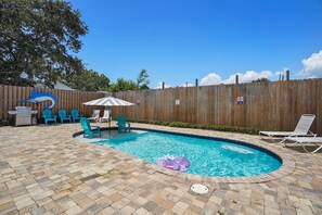 Un patio trasero con piscina, sillas de descanso y una parrilla.