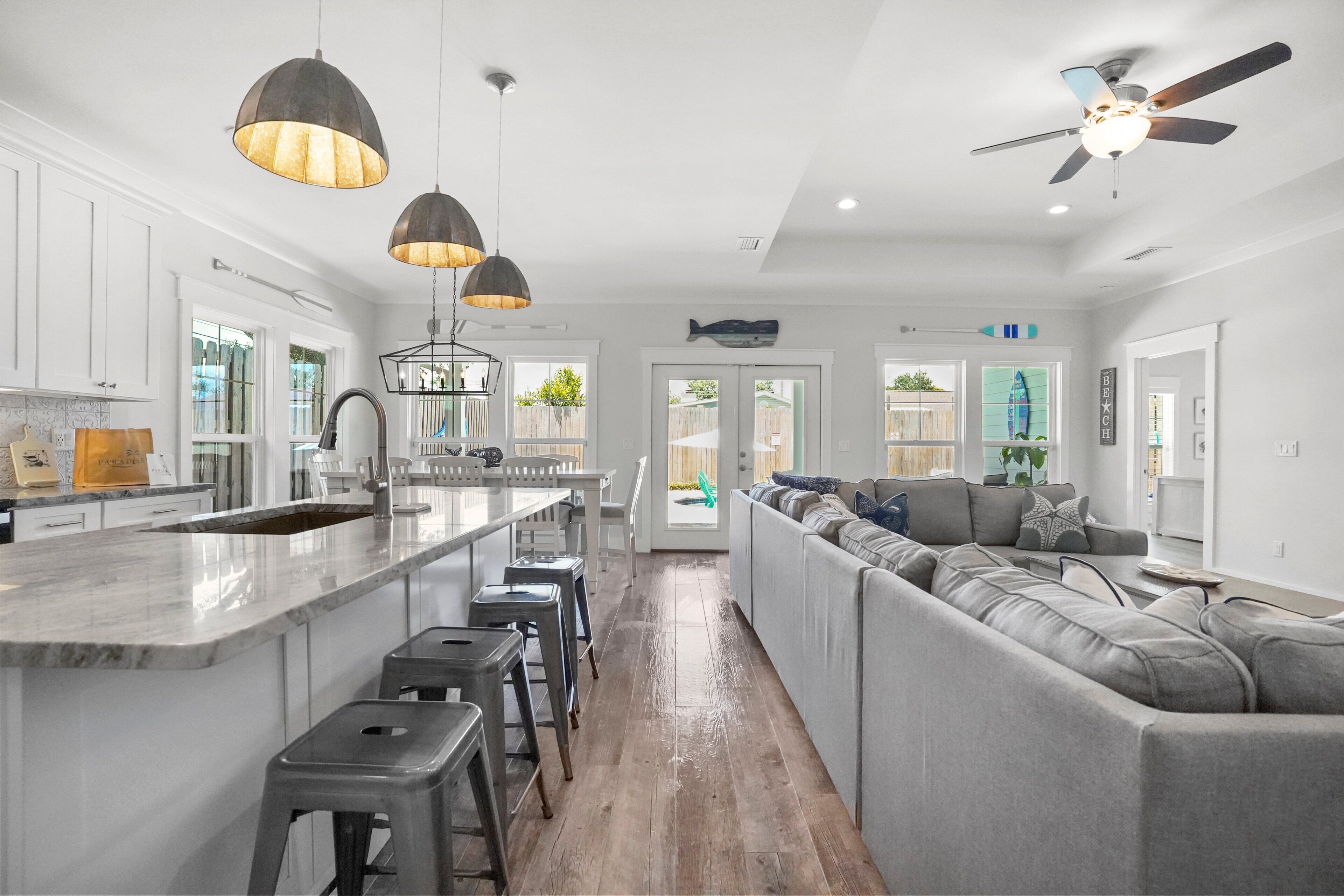 A modern kitchen with a central island, bar stools, pendant lighting, and a ceiling fan.