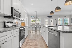 A modern kitchen with white cabinetry, a central island, stainless steel appliances, pendant lighting, and a view to the outside. - Caribbean Surf | Private Heatable Pool | Beach Access | PCB | Near Beach (Panama City Beach)