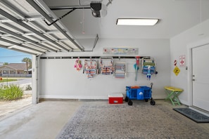 Un garaje con ventilador de techo, botiquín de primeros auxilios en la pared, nevera roja y carro azul.