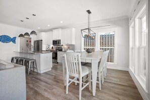 A modern kitchen with white cabinetry, stainless steel appliances, and a dining area with white chairs. - Caribbean Surf | Private Heatable Pool | Beach Access | PCB | Near Beach (Panama City Beach)