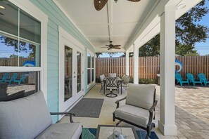 Ein überdachter Patio-Bereich mit Gartenmöbeln, Deckenventilator und Blick auf den Garten.
