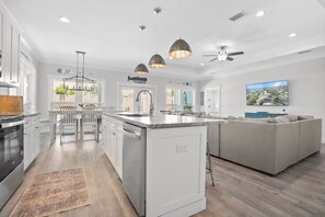 Una cocina moderna con muebles blancos, una isla central, iluminación colgante y un comedor con sillas.