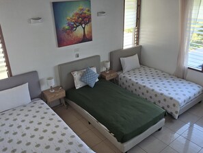 A room with two single beds, a nightstand with a lamp, a painting on the wall, and a window with blinds. - Seawinds Aura :House with spectacular ocean views and enormous balcony (Maui Bay, Coral Coast)
