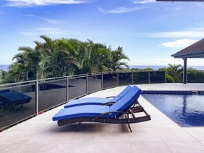 A poolside area with a lounge chair and a glass railing overlooking a body of water and palm trees. - Seawinds Aura :House with spectacular ocean views and enormous balcony (Maui Bay, Coral Coast)