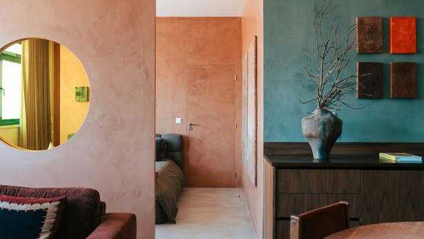 Un interior moderno con una mesa de comedor redonda, un sofá y una zona de cocina con un jarrón de ramas.
