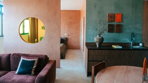 Un interior moderno con un espejo redondo, un sofá con un cojín estampado, una zona de comedor con una silla y una cocina con un florero en la encimera.