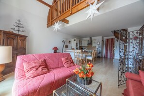 Una sala de estar con un sofá rojo, una mesa de centro de vidrio con flores, muebles de madera y una escalera.