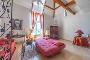 A room with a bed, a wooden cabinet, a table with a lamp, and a window with curtains. - Duplex de charme dans château de Beuzeval - Welkeys (Houlgate)