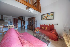 A living room with a wooden staircase, a dining area, and a bedroom with a bed and a painting. - Duplex de charme dans château de Beuzeval - Welkeys (Houlgate)