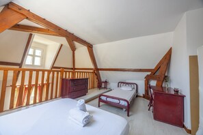 A bedroom with a sloped ceiling, wooden beams, a bed, a dresser, and a small table. - Duplex de charme dans château de Beuzeval - Welkeys (Houlgate)