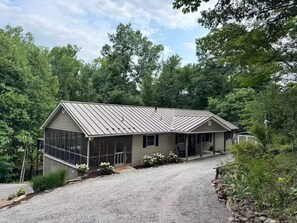 A single-story house with a metal roof, a covered porch, and a gravel driveway. - Modern Riverfront Retreat - Hot Tub & Fire Pit - Minutes from Berkley Springs (Great Cacapon)