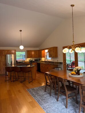 A spacious kitchen with wooden cabinets, a central island, and a dining area with a large table and chairs. - Modern Riverfront Retreat - Hot Tub & Fire Pit - Minutes from Berkley Springs (Great Cacapon)