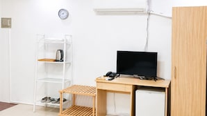 Pieni huone, jossa on työpöytä, televisio, hylly, jossa on vedenkeitin, ja pieni jääkaappi.