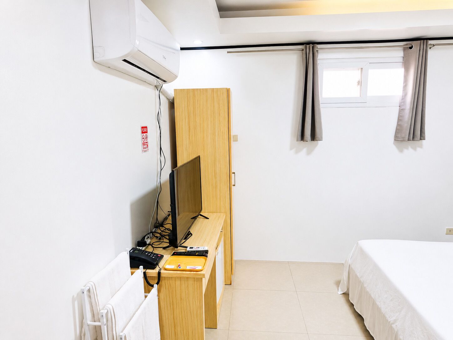 Ein Hotelzimmer mit Bett, Schreibtisch mit Computer, Klimaanlage und einem Fenster mit Vorhängen.