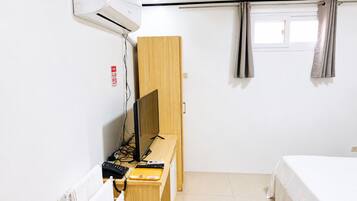 Ein Hotelzimmer mit Bett, Schreibtisch mit Computer, Klimaanlage und einem Fenster mit Vorhängen.