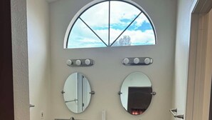 Ein Badezimmer mit Waschtisch, zwei Spiegeln, einem Fenster und einer Tür.