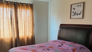 Ein Schlafzimmer mit einem Bett, einem Kopfteil, einem Fenster mit Vorhängen und einem an der Wand befestigten Schild.