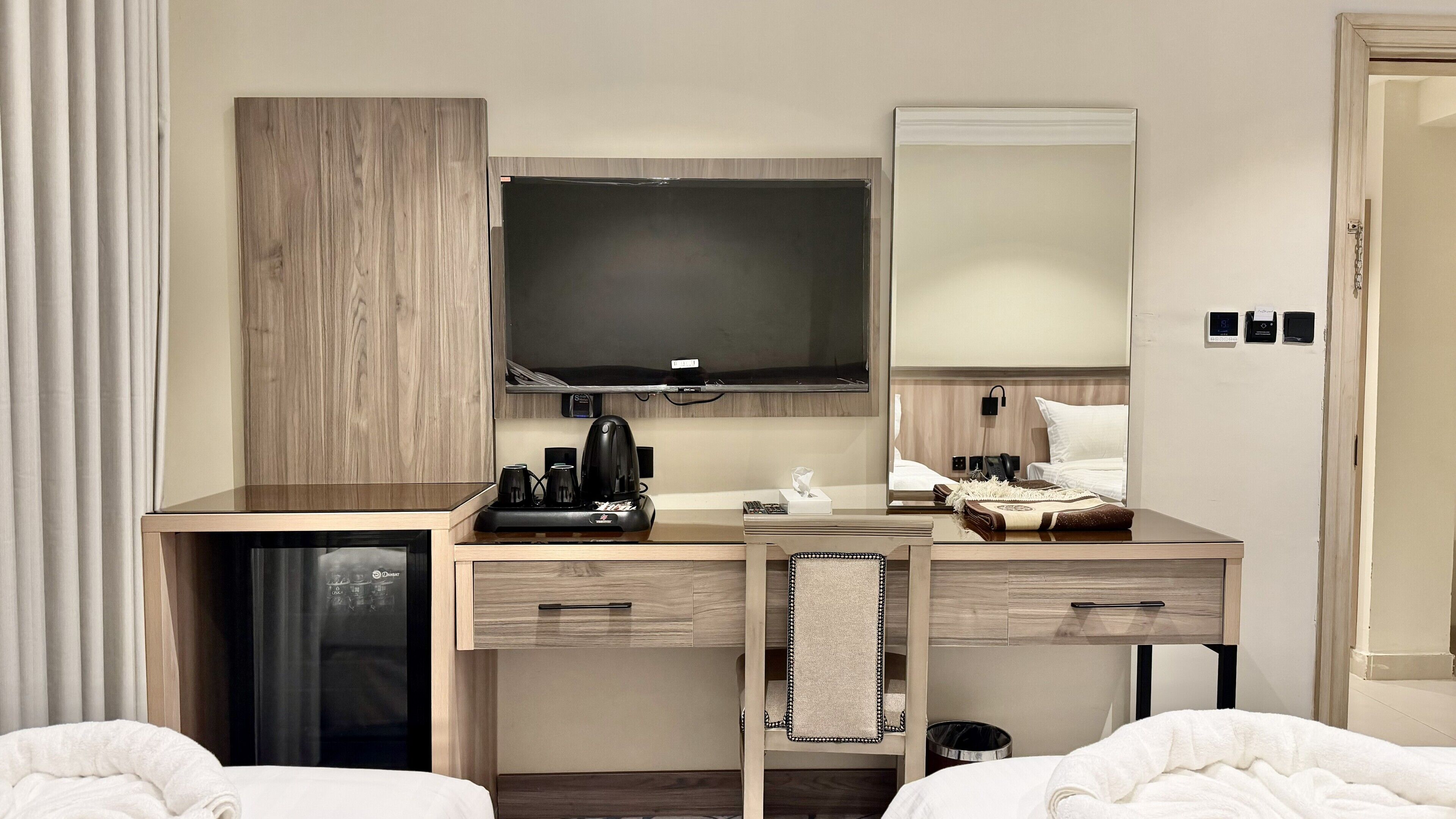 Ein Hotelzimmer mit Schreibtisch, Fernseher, Spiegel, Bett und einer kleinen Mülltonne.