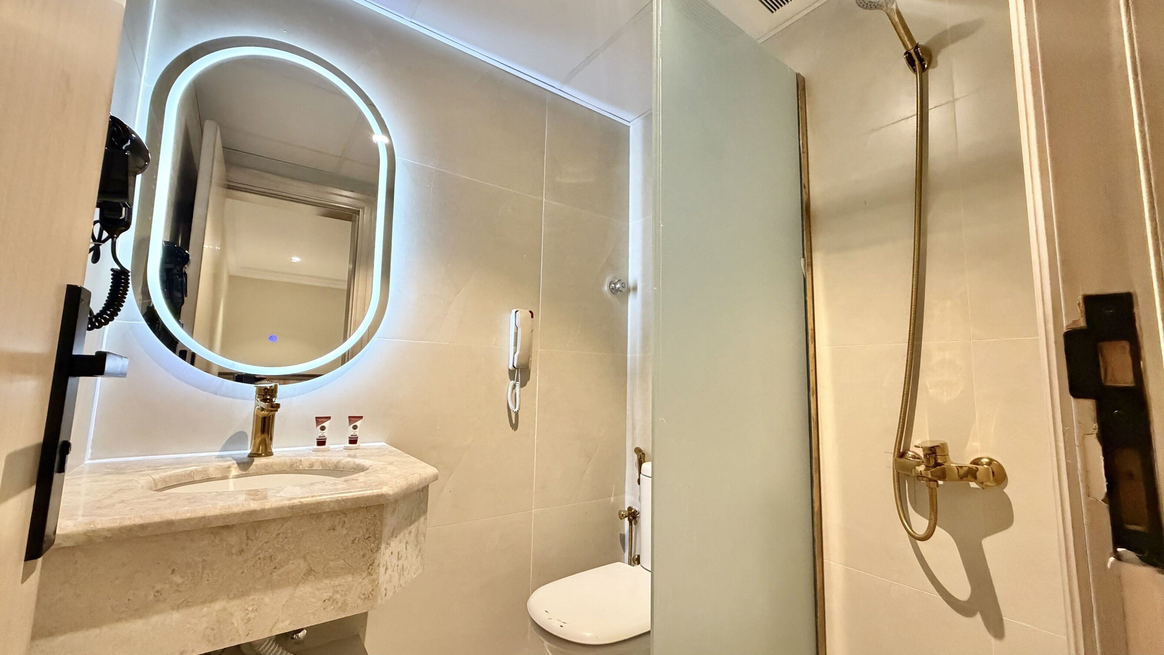 Ein Badezimmer mit Marmorwaschbecken, Toilette, Dusche inklusive Handbrause und einem an der Wand befestigten Telefon.