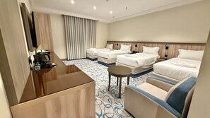 Een hotelkamer met een bed, twee slaapbanken, een kleintje tafeltje, een koffieapparaat en een televisie.