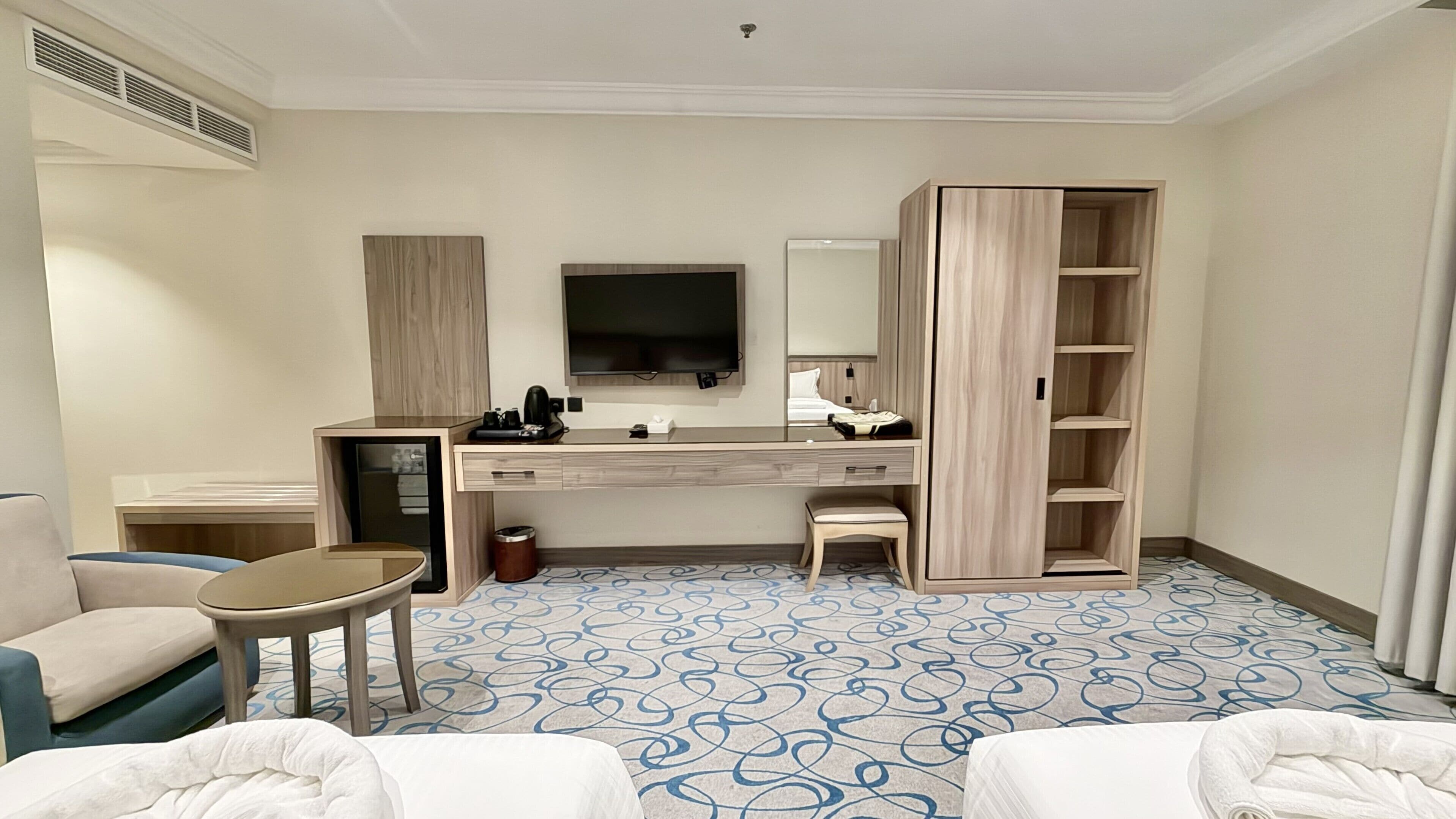 A hotel room with a large bed, a desk, a television, a wardrobe, and a patterned floor.