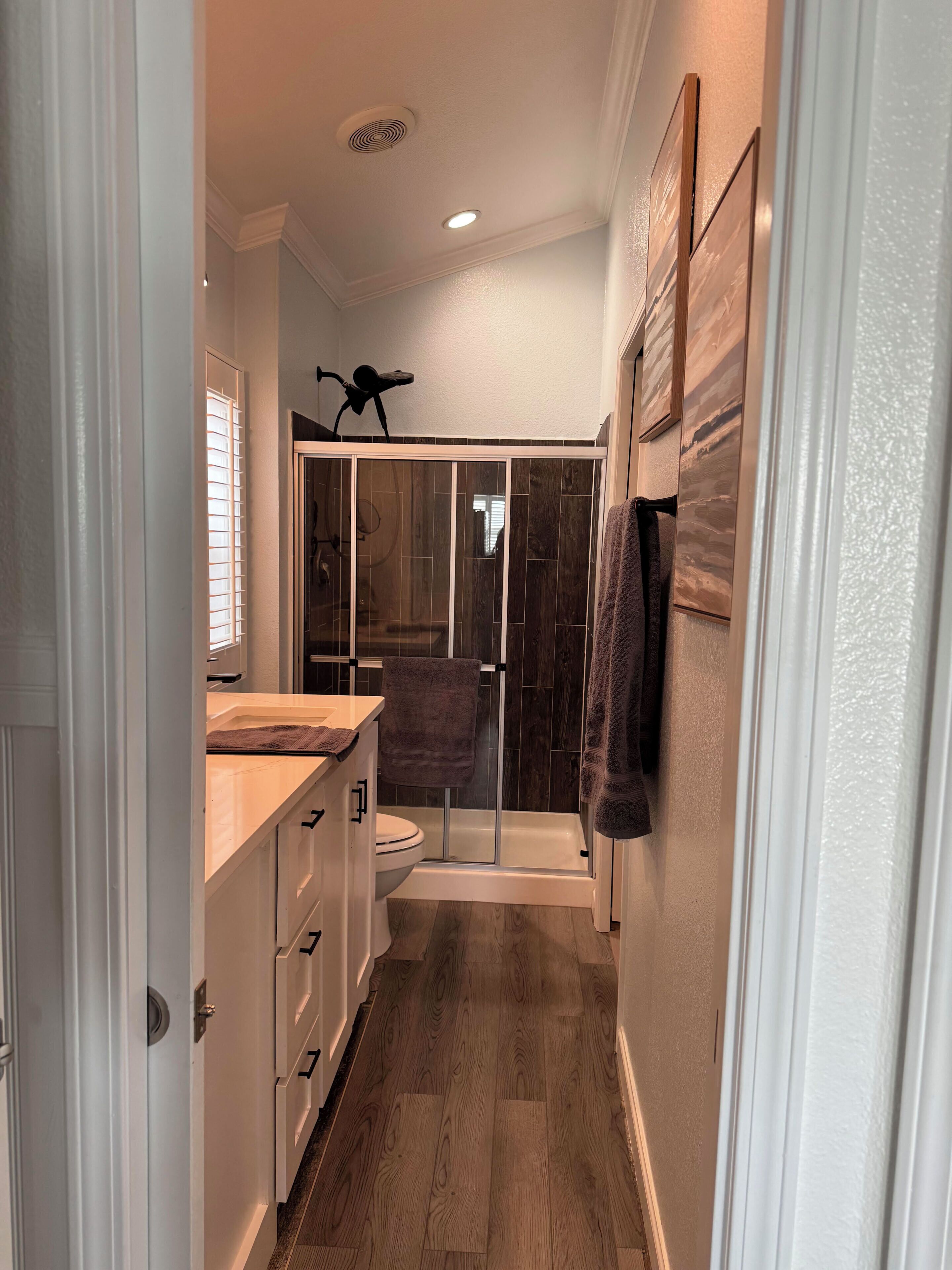 A narrow hallway leading to a bathroom with a shower, a toilet, and a sink.