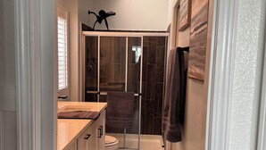 A narrow hallway leading to a bathroom with a shower, a toilet, and a sink.