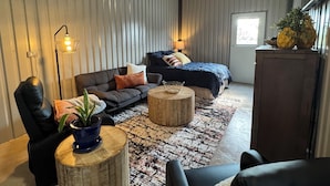 A modern living room with a sofa, a round coffee table, and a bed with a dark blue bedspread.