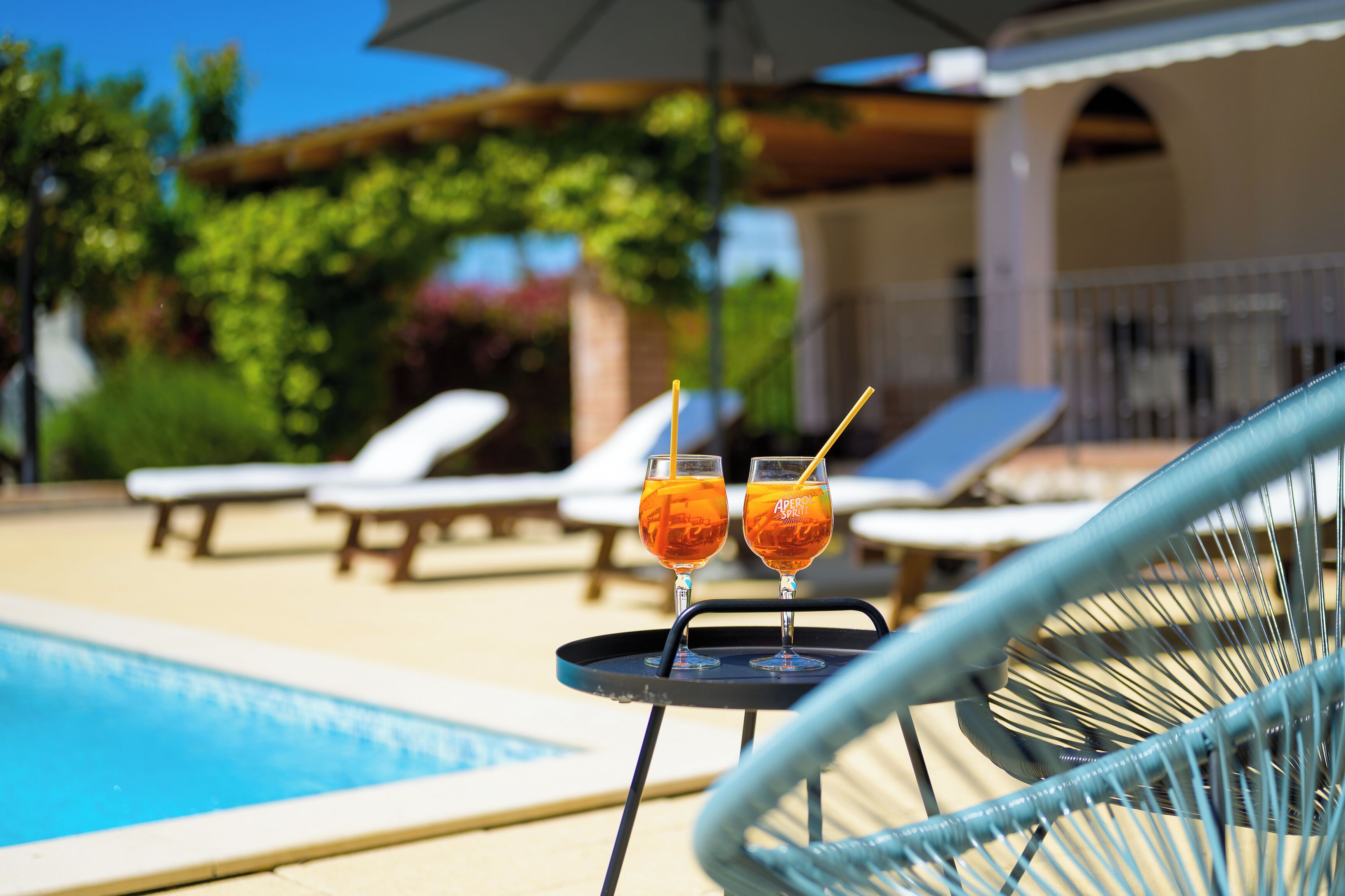 A poolside area with lounge chairs and two glasses of a beverage on a tray.