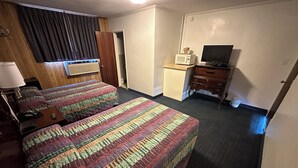 A hotel room with two beds, a desk, a microwave, a television, and a wardrobe.