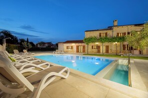 Une piscine avec des chaises longues et, en arrière-plan, un bâtiment en pierre.