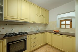 A kitchen with yellow cabinets, a gas stove, a sink, and a window with a view. - Villa Marija Pekici (Istria - Svetvinčenat) (Svetvinčenat)