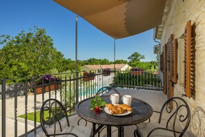 Een balkon met een tafel voor twee, compleet met croissants en een rode roos.