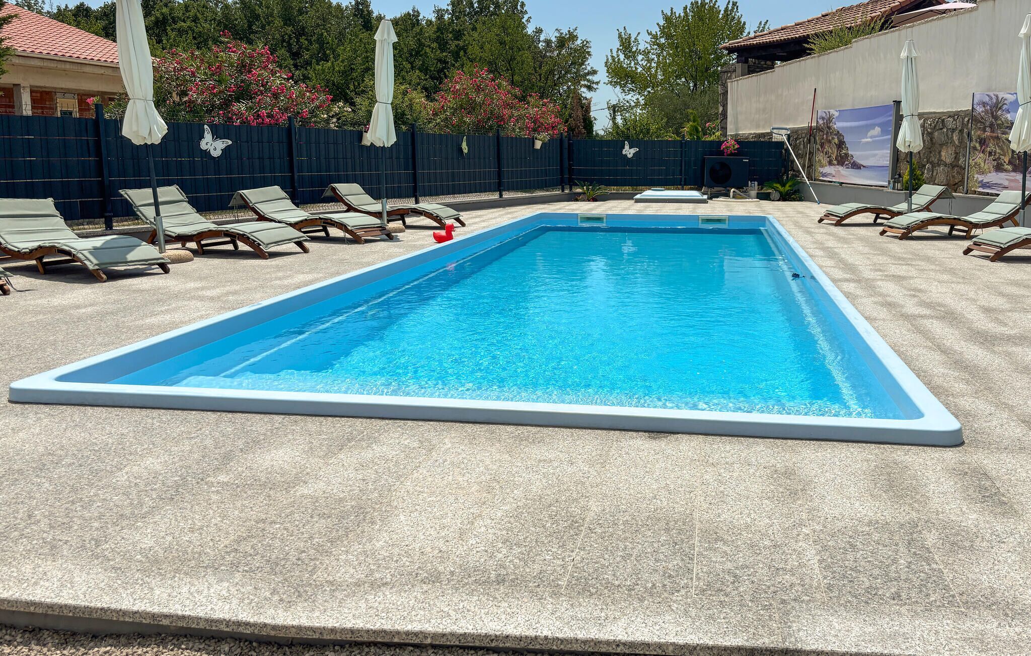 Ein rechteckiger Swimmingpool mit weißer Umrandung, umgeben von Liegestühlen und Sonnenschirmen.
