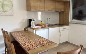 A kitchen with wooden cabinets, a countertop, a sink, a coffee maker, and a dining table with a unique wood pattern. - Awesome apartment in Opric (Opric)