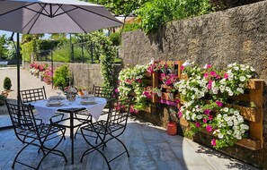 An outdoor patio with a round table set for dining, surrounded by chairs, and a large umbrella providing shade. - Awesome apartment in Opric (Opric)