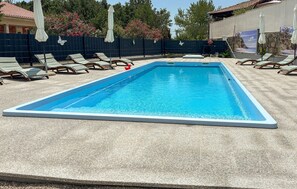 Una piscina rettangolare con bordo bianco, circondata da sdraio e ombrelloni.
