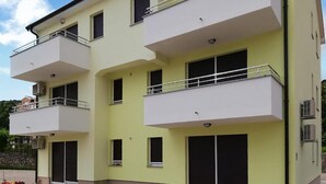 Un edificio residencial de varios pisos con balcones, unidades de aire acondicionado y un cielo despejado.