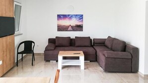 Una sala de estar con sofá seccional, una mesita, un sillón y televisor instalado en la pared.