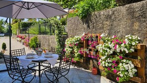 Un patio al aire libre con una mesa redonda dispuesta para comer, rodeada de sillas y un gran paraguas que da sombra.