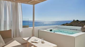 Een balkon met uitzicht op zee, een jacuzzi, een tafel met een boek en glazen, en een bank.
