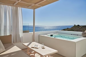 A balcony with a view of the sea, a hot tub, a table with a book and glasses, and a sofa.