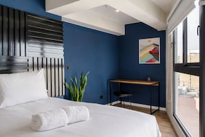 Ein Hotelzimmer mit Bett, Schreibtisch, Stuhl, Blumentopf und Fenster.