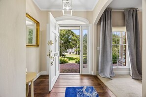 A hallway with a wooden floor, a blue rug, a white door leading outside, and a view of a brick patio and greenery. - Waterfront Amelia Island home with amazing views, deck, parking. (Fernandina Beach)
